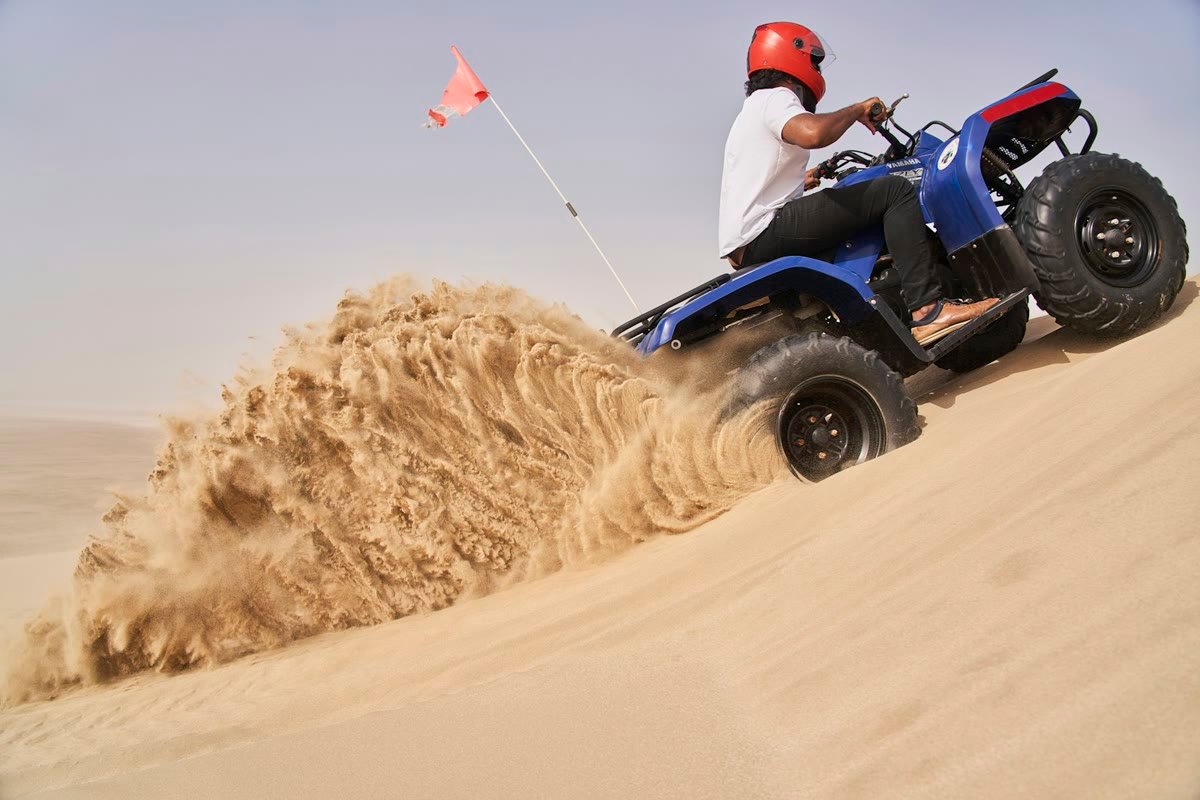 Quad bike kicking up a large cloud of sand on a desert dune